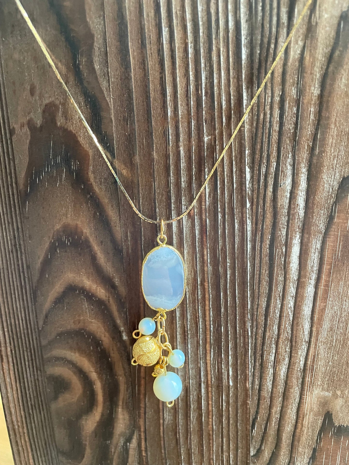 Agate, Opalite, and 18K gold beaded pendant necklace. It is hanging on a wooden board.