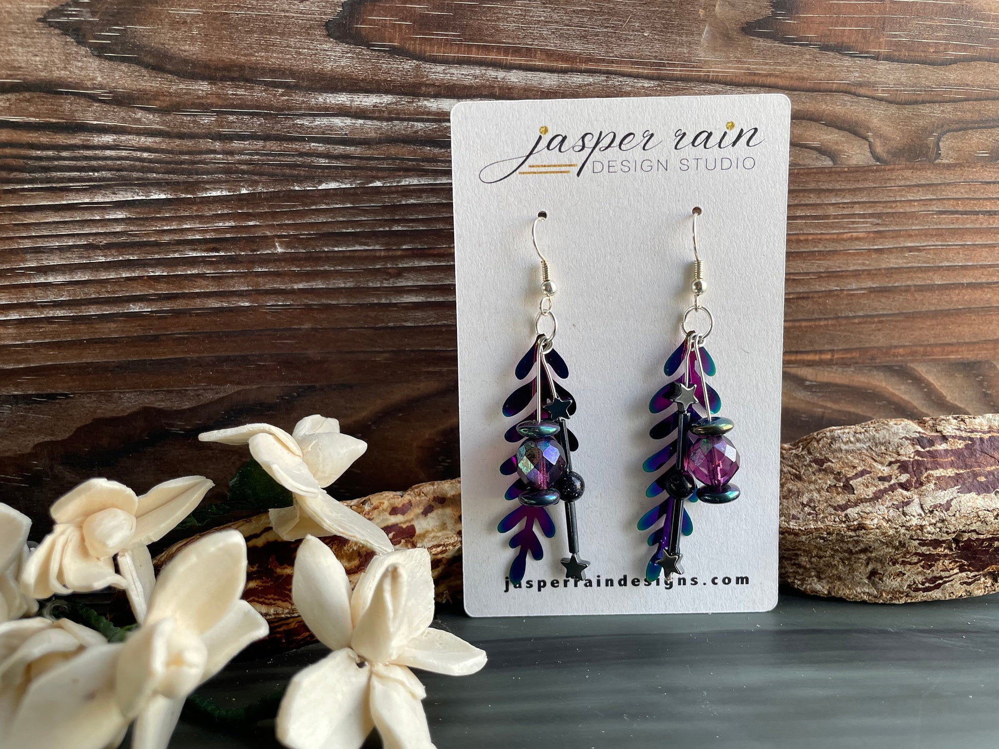 Colorful rainbow dangle earrings that are handmade and feature hematite stone stars and a metal rainbow leaf