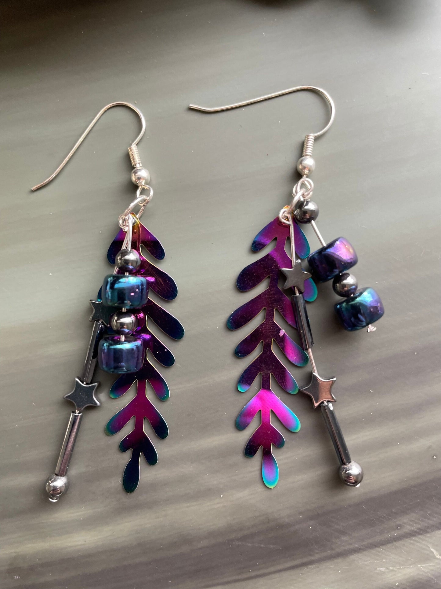 Colorful rainbow dangle earrings that are handmade and feature hematite stone stars and a metal rainbow leaf