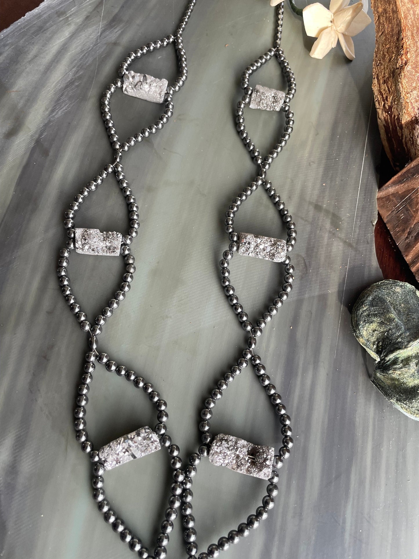 Platinum Druzy and Hematite long length necklace sitting on a stone tablet